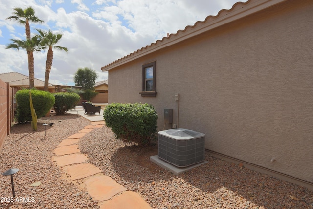 view of side of property with a patio, fence, central AC, and stucco siding