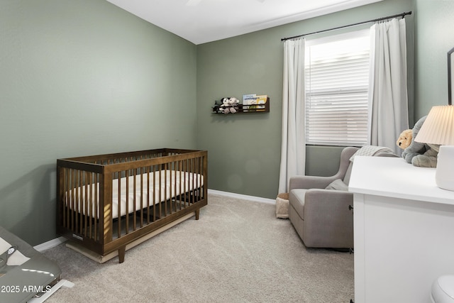 bedroom featuring light colored carpet, ceiling fan, and a nursery area