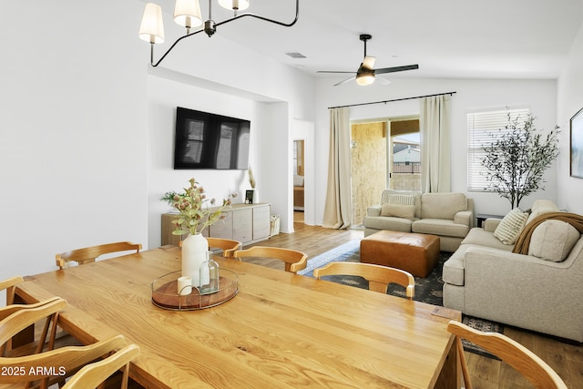 dining room featuring hardwood / wood-style floors, ceiling fan with notable chandelier, and vaulted ceiling