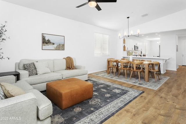 living room with light wood-type flooring, vaulted ceiling, ceiling fan with notable chandelier, and sink