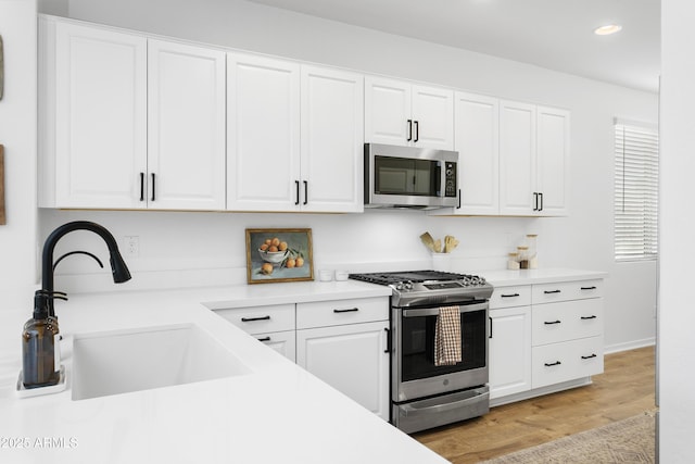 kitchen with sink, light wood-type flooring, white cabinetry, and appliances with stainless steel finishes