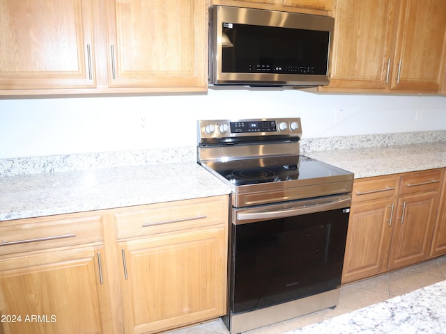 kitchen featuring light tile patterned flooring, light stone counters, and appliances with stainless steel finishes