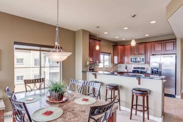 kitchen featuring sink, hanging light fixtures, kitchen peninsula, stainless steel appliances, and decorative backsplash