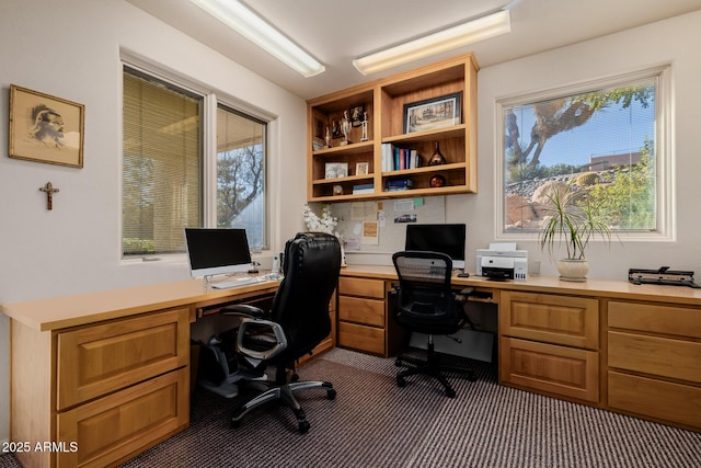 home office featuring a healthy amount of sunlight, built in desk, and dark colored carpet