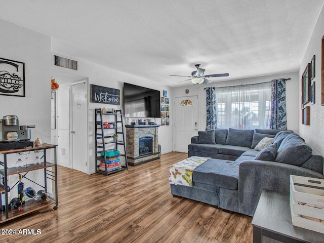 living room featuring hardwood / wood-style flooring, ceiling fan, a fireplace, and a textured ceiling