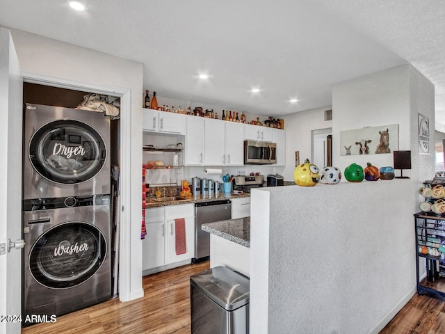 kitchen with white cabinetry, light hardwood / wood-style flooring, stacked washer and dryer, dark stone counters, and appliances with stainless steel finishes