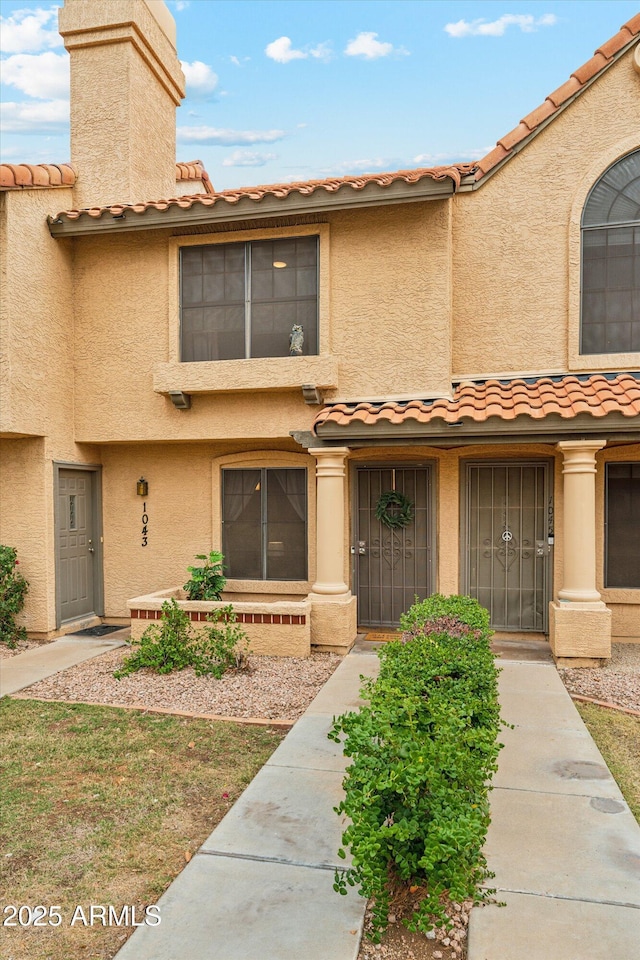 view of property featuring stucco siding, a chimney, and a tiled roof