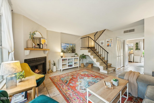 tiled living area with visible vents, a lit fireplace, and stairs