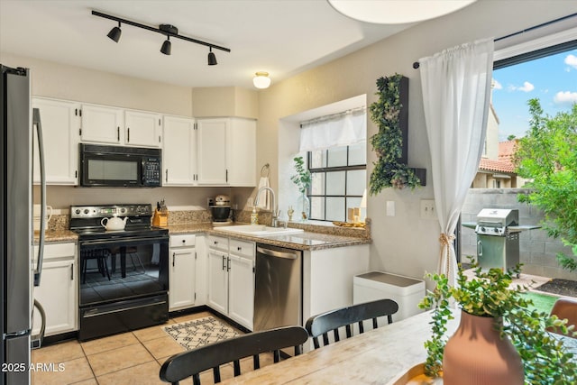 kitchen featuring tile counters, light tile patterned floors, white cabinets, black appliances, and a sink