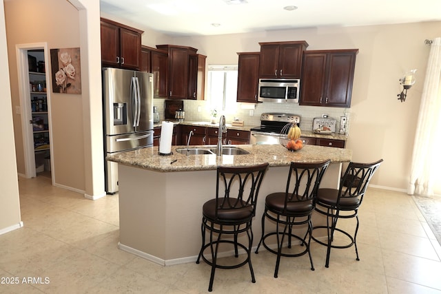 kitchen with tasteful backsplash, a sink, a kitchen island with sink, dark brown cabinetry, and stainless steel appliances