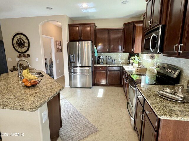 kitchen with light stone counters, a sink, arched walkways, backsplash, and appliances with stainless steel finishes