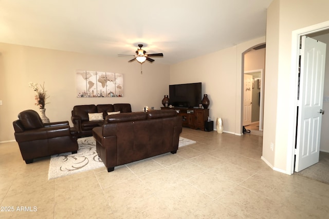 living area featuring a ceiling fan, baseboards, arched walkways, and light tile patterned floors