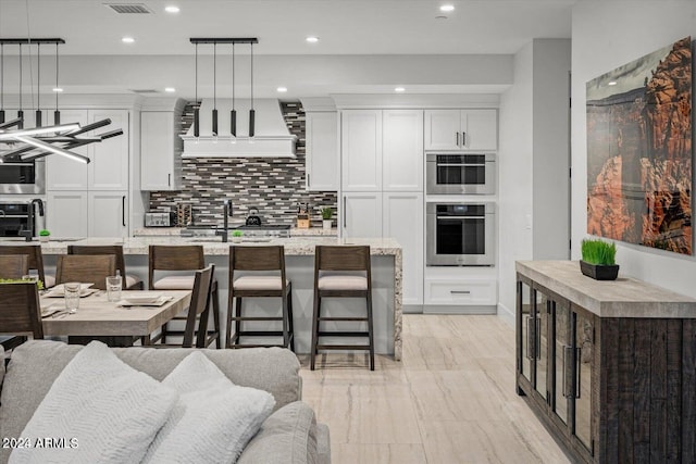 kitchen with white cabinets, a center island with sink, hanging light fixtures, and a kitchen breakfast bar