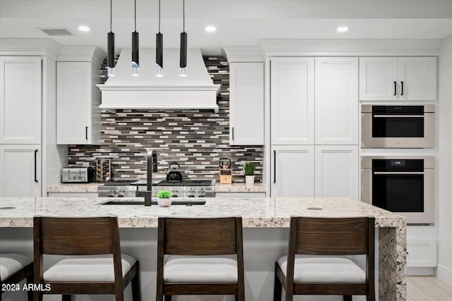 kitchen featuring custom range hood, white cabinets, decorative light fixtures, and a breakfast bar