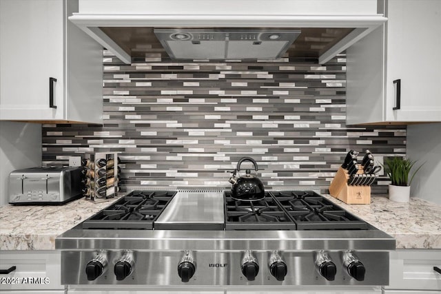 kitchen with backsplash, stainless steel stove, light stone counters, and white cabinetry