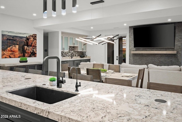 kitchen with light stone countertops, hanging light fixtures, sink, and decorative backsplash