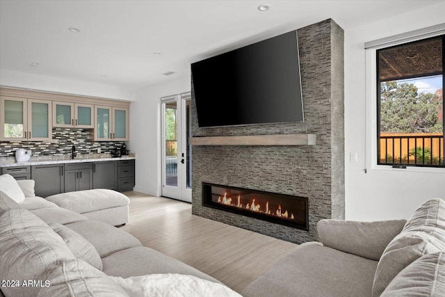 living room featuring wet bar, light wood-type flooring, a wealth of natural light, and a stone fireplace