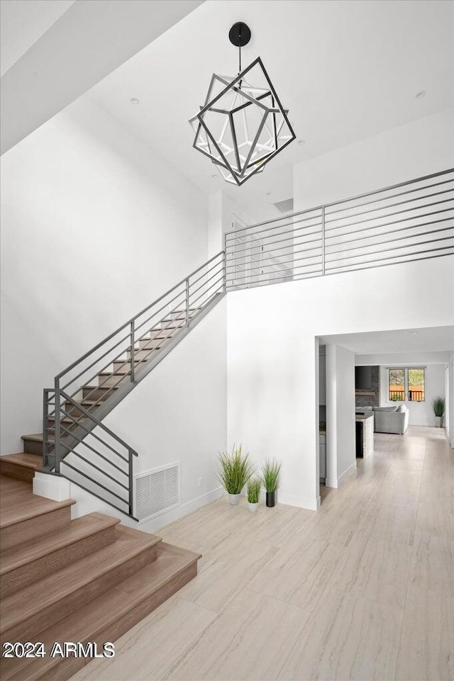 stairway with an inviting chandelier, hardwood / wood-style flooring, and a towering ceiling