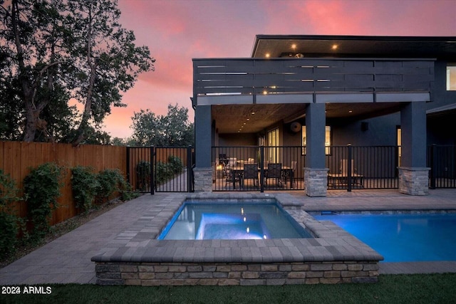 pool at dusk featuring a patio and an in ground hot tub