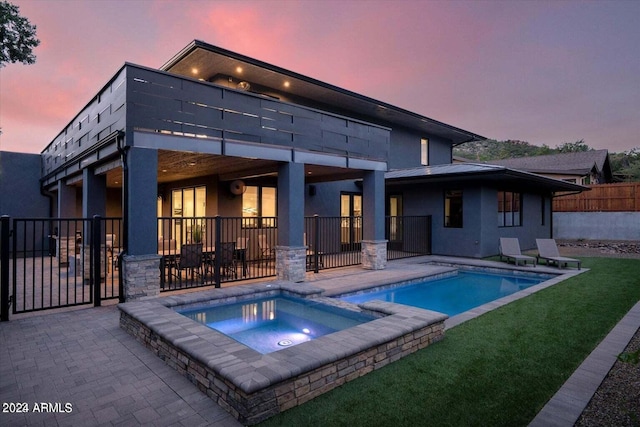 back house at dusk featuring a yard, a pool with hot tub, and a patio