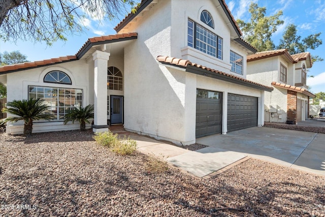 mediterranean / spanish-style home featuring an attached garage, driveway, a tiled roof, and stucco siding