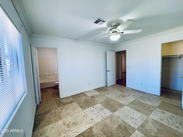 unfurnished bedroom featuring ornamental molding, stone tile flooring, baseboards, and a walk in closet