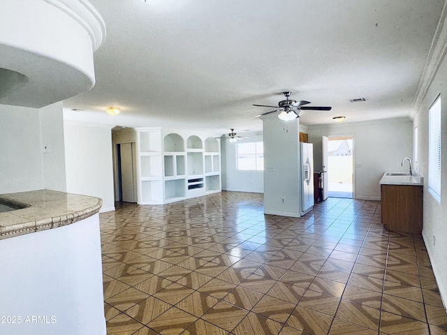 unfurnished living room featuring ceiling fan, crown molding, baseboards, and a sink