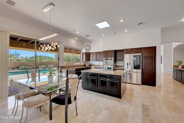 kitchen with appliances with stainless steel finishes, pendant lighting, dark brown cabinets, a center island, and a skylight