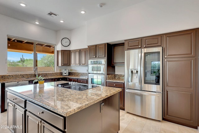 kitchen featuring dark brown cabinetry, sink, stainless steel appliances, a center island, and light stone countertops