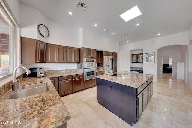 kitchen with a kitchen island, light stone countertops, stainless steel appliances, a skylight, and sink