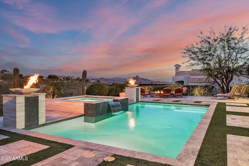 pool at dusk featuring a fire pit, an in ground hot tub, and a patio area