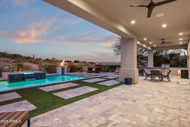 pool at dusk featuring a patio area, ceiling fan, an in ground hot tub, and area for grilling