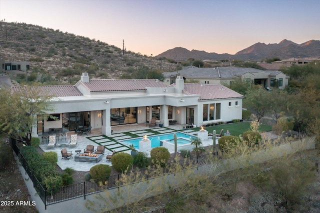 back house at dusk with an outdoor fire pit, a mountain view, a fenced in pool, and a patio