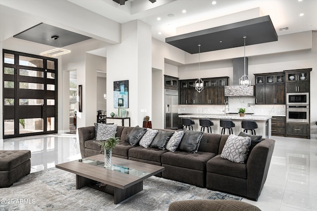 tiled living room featuring sink, a high ceiling, and a chandelier