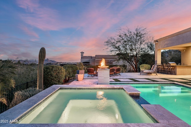 pool at dusk featuring a patio area, a bar, an outdoor fire pit, area for grilling, and an in ground hot tub