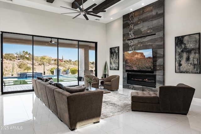 living room with a tiled fireplace, beam ceiling, ceiling fan, and a healthy amount of sunlight