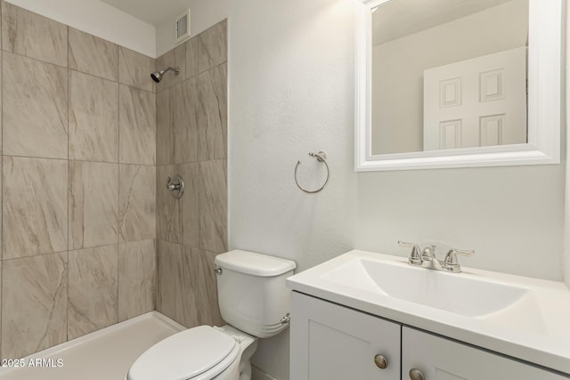 bathroom with tiled shower, vanity, and toilet