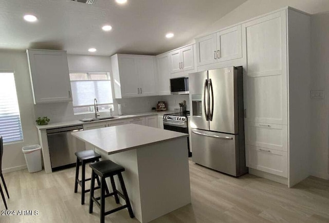 kitchen with sink, a center island, a breakfast bar, white cabinetry, and appliances with stainless steel finishes