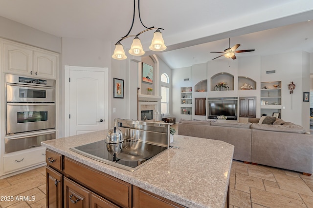 kitchen featuring a warming drawer, stainless steel double oven, ceiling fan, black electric stovetop, and a glass covered fireplace