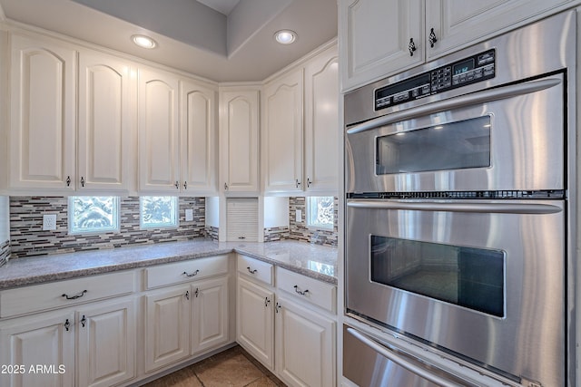 kitchen with double oven, a warming drawer, decorative backsplash, and white cabinetry