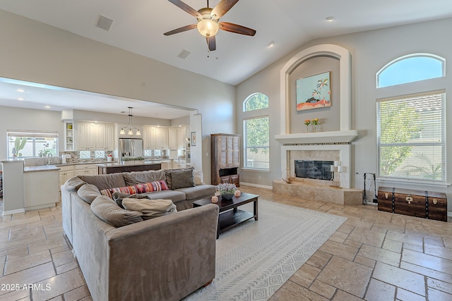 living room featuring stone tile flooring, high vaulted ceiling, baseboards, and ceiling fan