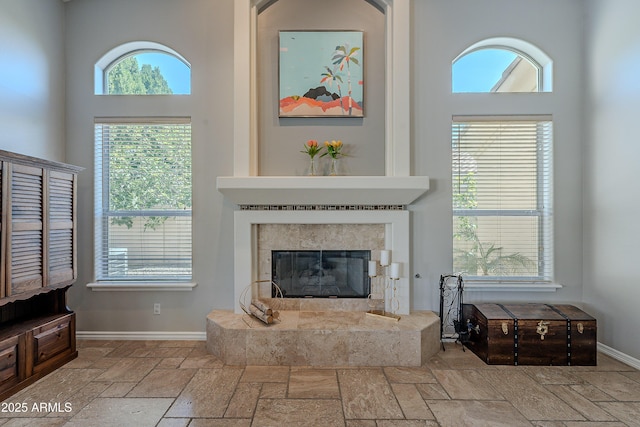 living area with baseboards, a tiled fireplace, and stone tile flooring