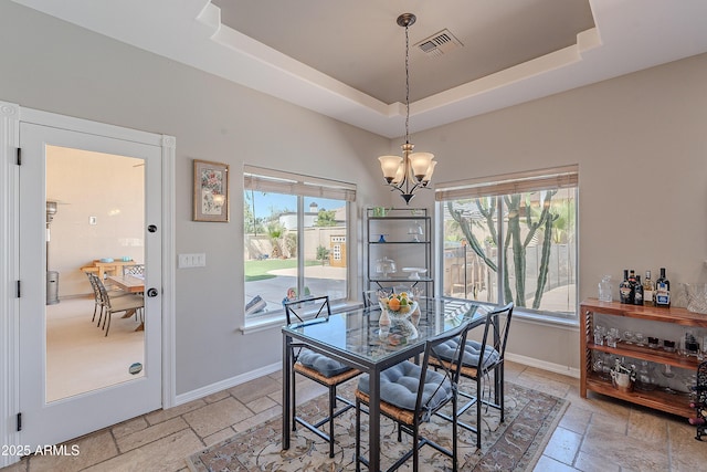 dining room featuring visible vents, baseboards, stone tile flooring, a tray ceiling, and an inviting chandelier