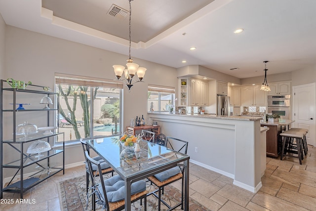dining room featuring a tray ceiling, visible vents, a healthy amount of sunlight, and stone tile floors