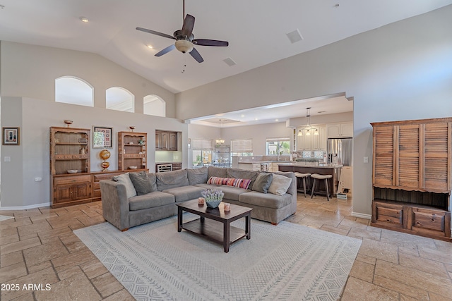 living room with high vaulted ceiling, stone tile floors, baseboards, visible vents, and ceiling fan