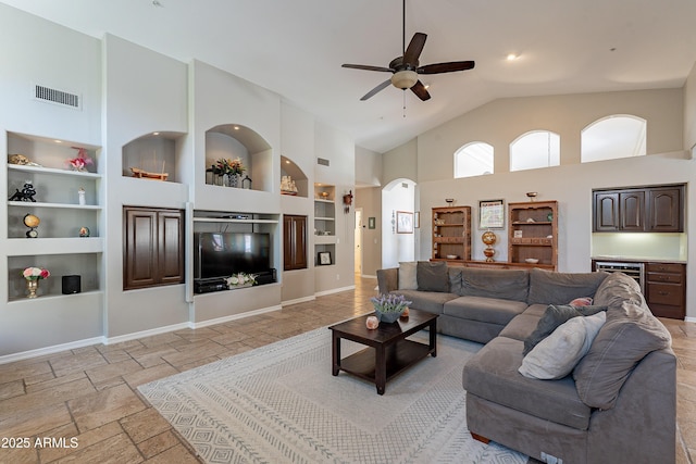 living area featuring high vaulted ceiling, built in shelves, visible vents, a ceiling fan, and stone tile flooring
