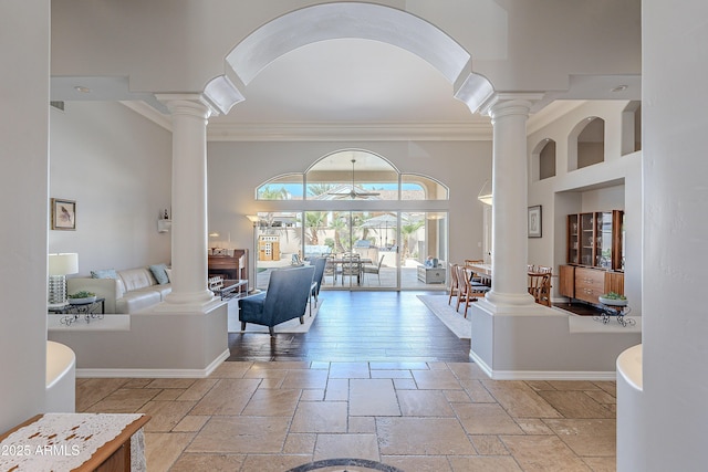 interior space featuring decorative columns, stone tile flooring, baseboards, and a towering ceiling
