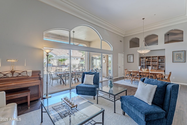 living room with baseboards, a towering ceiling, wood finished floors, and crown molding