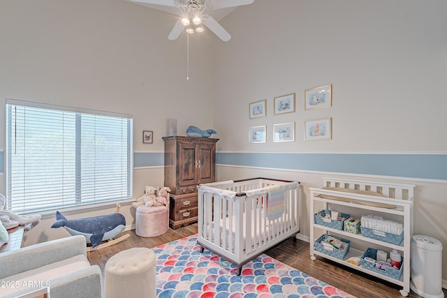 bedroom featuring a towering ceiling, wood finished floors, a crib, and a ceiling fan