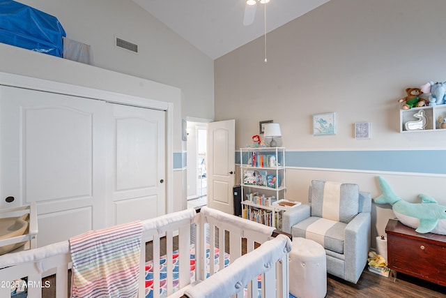 bedroom with high vaulted ceiling, visible vents, a crib, a closet, and wood finished floors